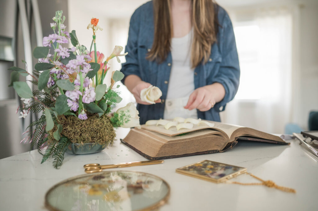 an artist in the kitchen with a bridal bouquet pressing petals in a book